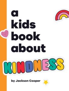 Book cover for "A Kids Book About Kindness" by Jackson Cooper, featuring a white background with an orange border on the left. “A Kids Book About” is displayed in black text with the word “KINDNESS” below as a sticker in colorful letters. Other stickers are scattered around the cover, including a rainbow, heart, and a star.