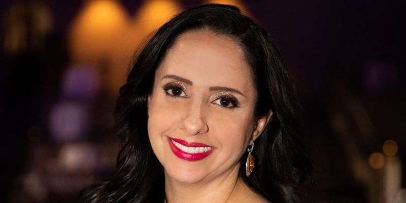 Headshot of Abby Jimenez (with tan skin, long black hair, red lipstick, and nude glitter eyeshadow)