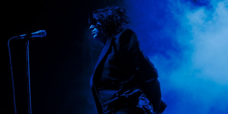 Arooj Aftab stands in front of a microphone on a stage with dark blue lighting and fog floating in the background.