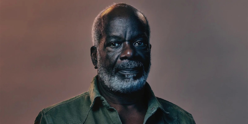 Headshot of Joseph Marcell (with dark skin, grey textured hair/beard, and green button-down shirt)