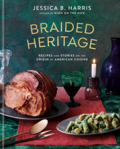 Book cover for "Braided Heritage: Recipes and Stories on the Origin of American Cuisine" by Jessica B. Harris, author of "High on the Hog." The cover features a tablescape with dark glassware, carved ham, and fried okra.