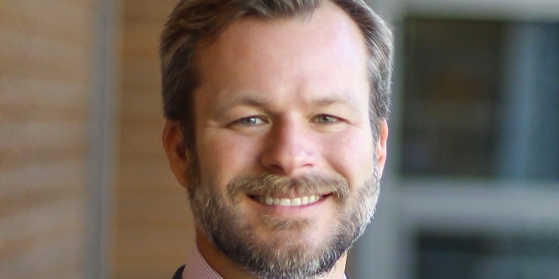 Headshot of Brian Soucek (with short dark blonde hair, beard, and suit)