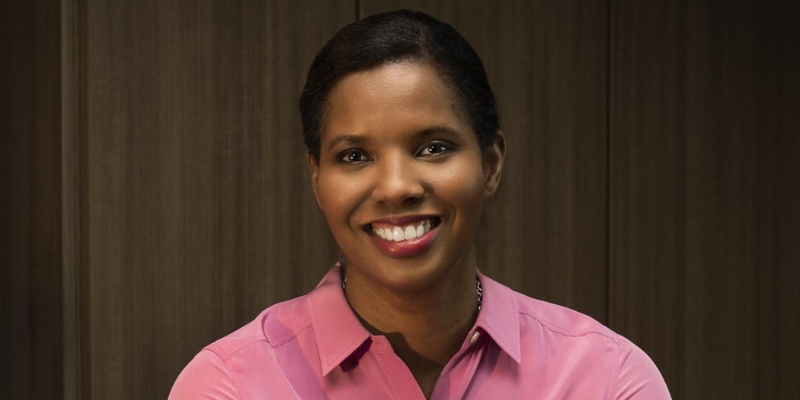 Headshot of Briana Scurry (with dark skin, black ponytail, and pink blouse)