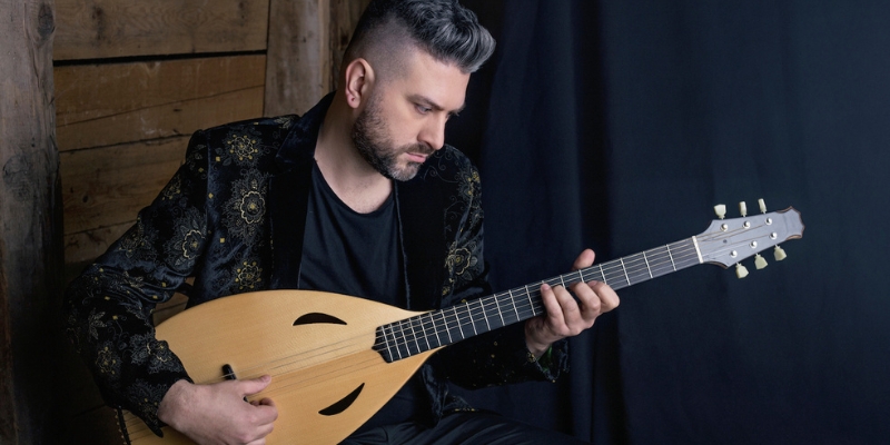 Damir Imamovic plays a string instrument similar to a lute, wearing a black jacket with gold intricate patterns.