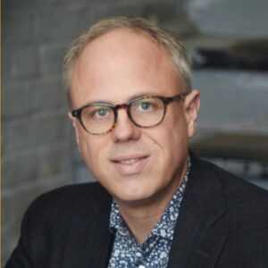Headshot of David Daley (with fair skin, short blonde hair, and tortoiseshell glasses)