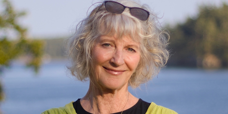 Headshot of Drew Harvell (with fair skin, blonde hair/bangs, and sunglasses worn as a headband)