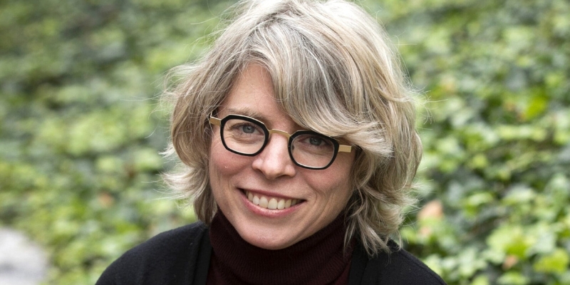 Outdoor headshot of Jill Lepore (with fair skin, wavy blonde bob, glasses, and black turtleneck)