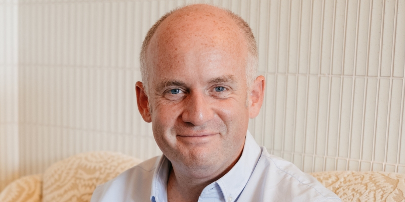 Headshot of Oliver Burkeman (with fair skin, bald haircut, and blue button-down shirt)