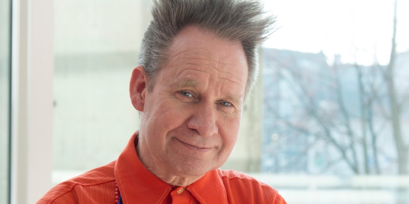 Headshot of Peter Sellars (with fair skin, spiked short grey hair, and orange button-down shirt)