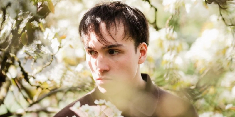 Headshot of Roman Goron (with fair skin and short brown hair) posing among cherry blossom trees.