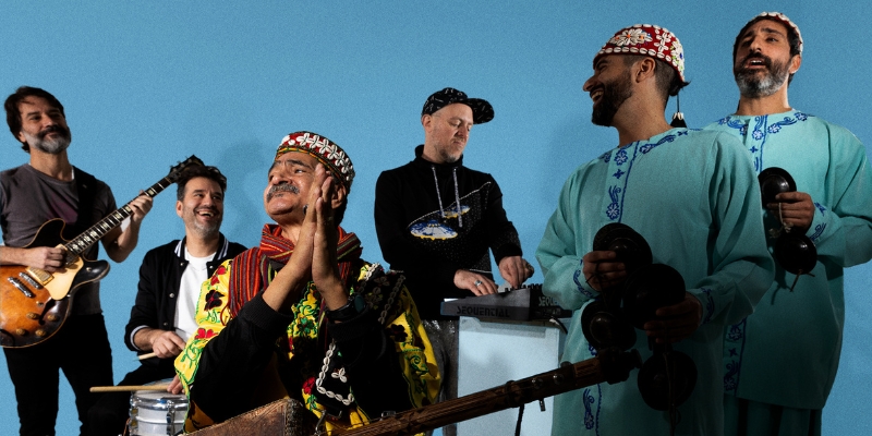 Group photo of Saha Gnawa holding their instruments in front of a blue background.