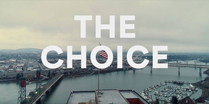 Banner graphic for "The Choice," featuring the title in bold white text overlaid a picture of a cityscape with a highway bridge over water.