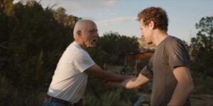 Patrick McCollum (with grey hair/mustache) and Gabe Polsky (with curly brown hair, green t-shirt) shake hands outdoors while the sun sets.