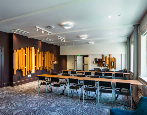 Photo of a small, carpeted room with windows and 2 long tables with chairs