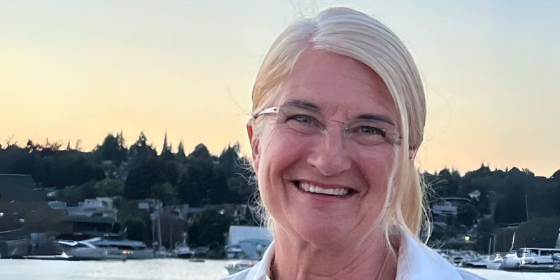 Wendy Norman in a white shirt and glasses stands in front of a body of water