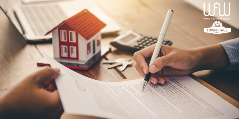 A person handing a form to another, who signs the bottom with a white pen. A model of a small house, keys, and a calculator are on the table next to the person signing. The Worry Free Wednesdays and Town Hall Seattle logo are in the upper right corner.