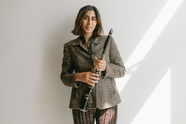 Jahnvi Madan poses and smiles holding her clarinet in front of a white wall.