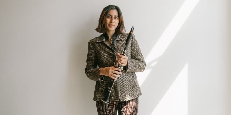 Jahnvi Madan poses and smiles holding her clarinet in front of a white wall.